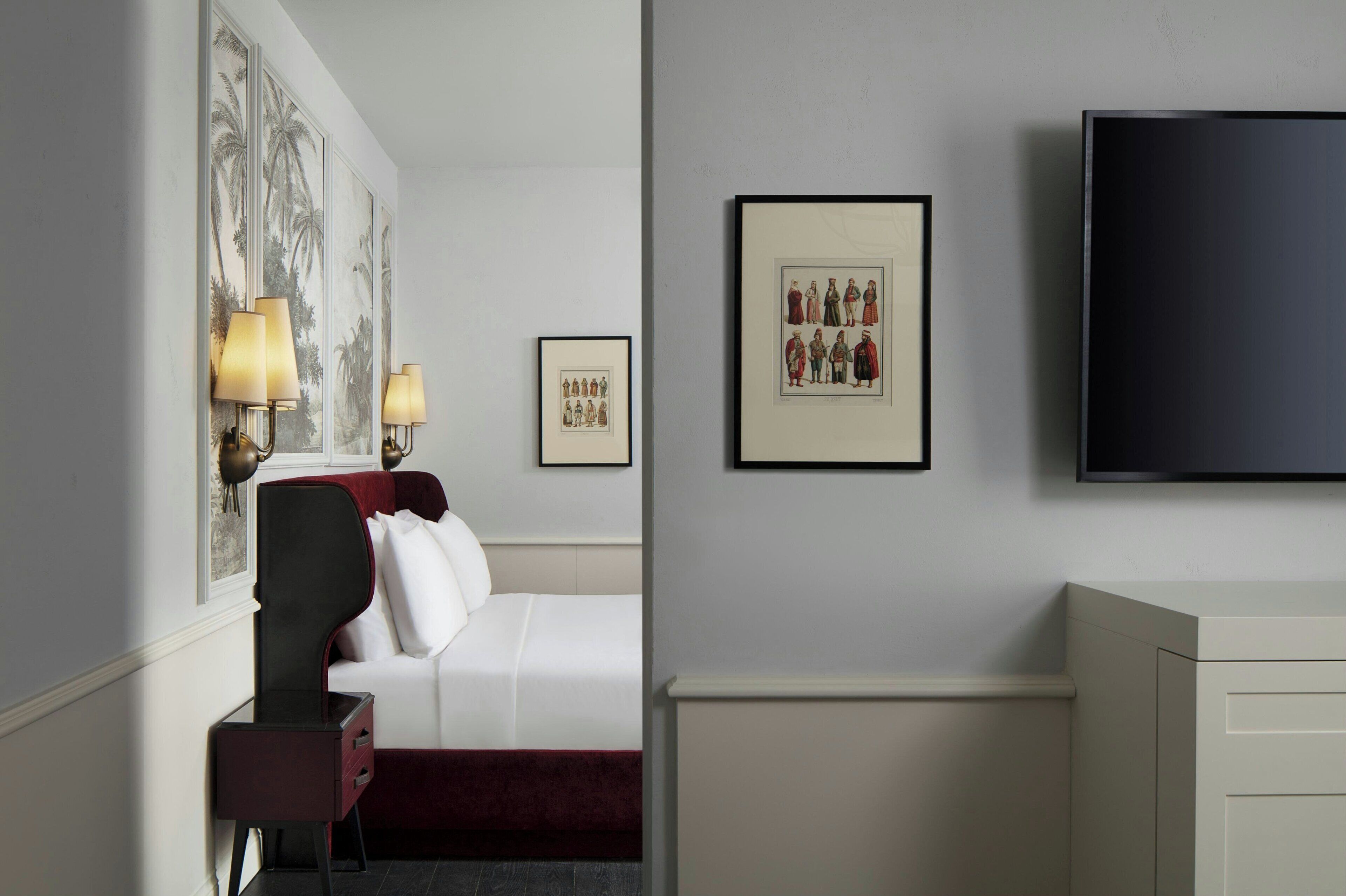 Ein Hotelzimmer mit Bett, Schreibtisch, Stuhl, Fernseher und gerahmten Bildern an der Wand.