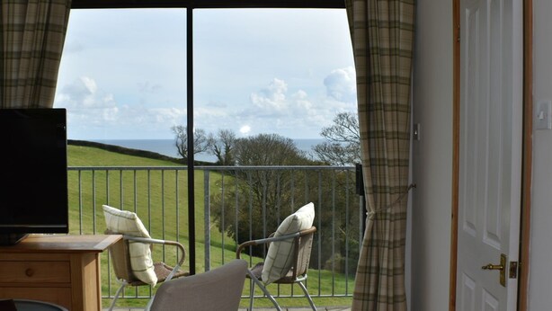 A balcony with two chairs and a TV, overlooking a grassy area and the sea.