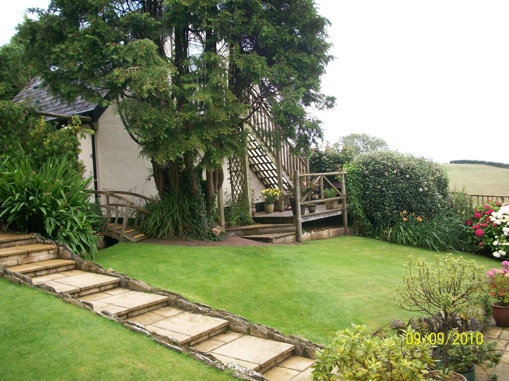 Ein Garten mit einer Steintreppe, die zu einer Holterrasse führt, umgeben von üppigem Grün und blühenden Pflanzen.