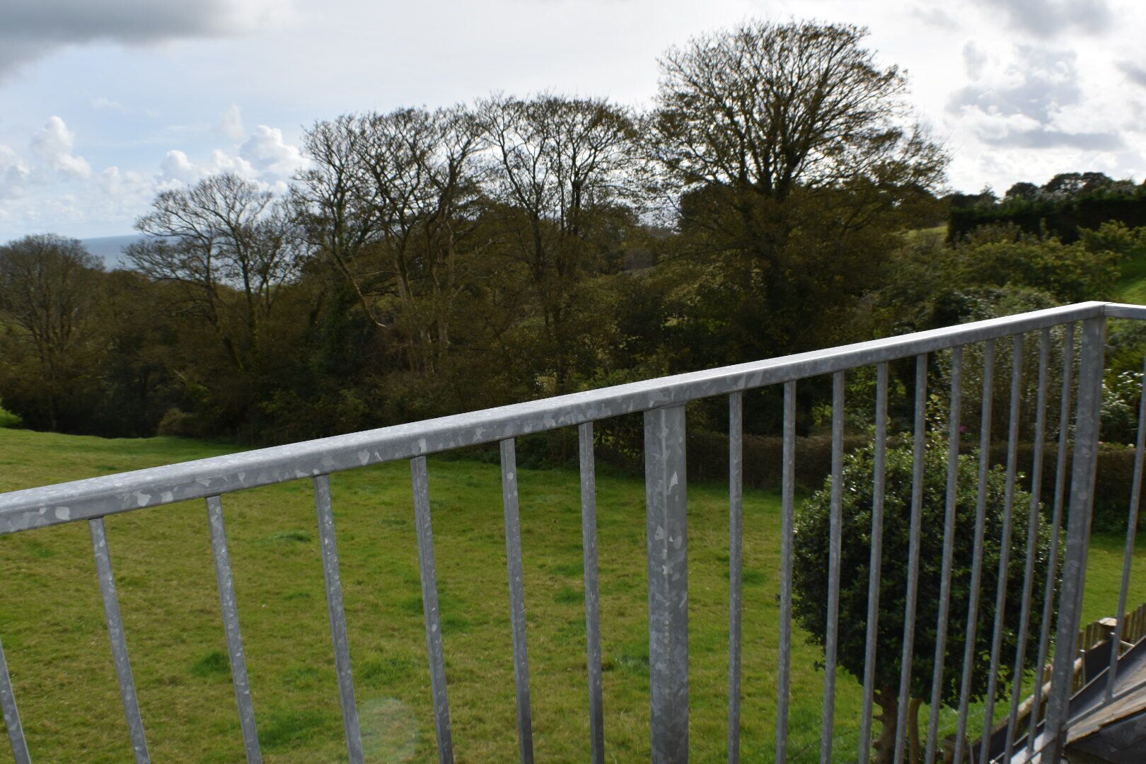 A metal railing overlooking a grassy field with trees in the background.