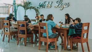 A restaurant with wooden tables and chairs, a sign reading "Hotel Loya", and a palm tree in the background. - Hostal Loja (Puerto Villamil)