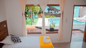 A hotel room with a bed, a view of a swimming pool, and a patio area with chairs and plants. - Hostal Loja (Puerto Villamil)