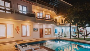 A two-story building with a swimming pool, lounge chairs, and a balcony. - Hostal Loja (Puerto Villamil)
