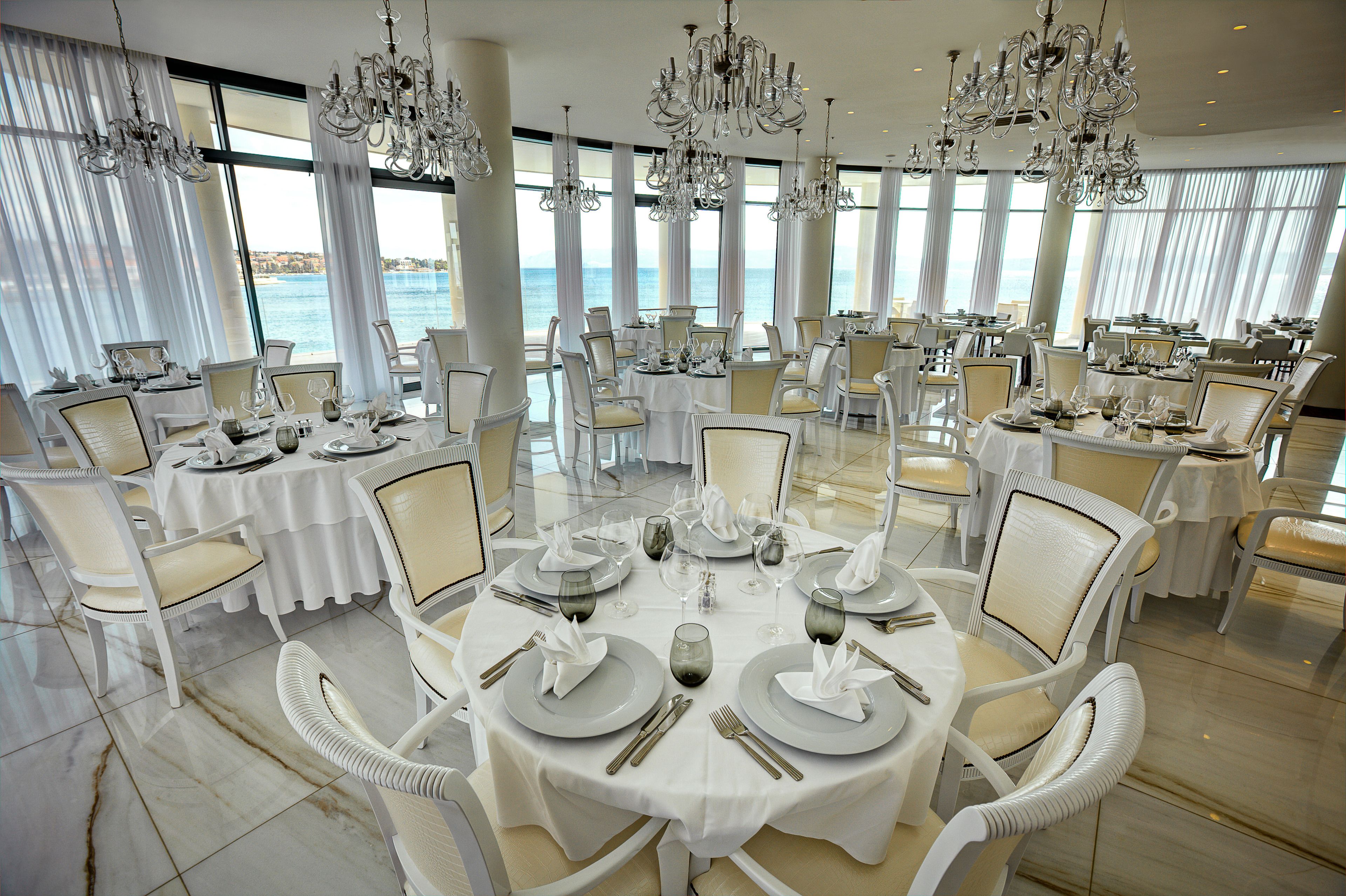 Een luxueuze eetruimte met ronde tafels, witte stoelen en elegante kroonluchters.