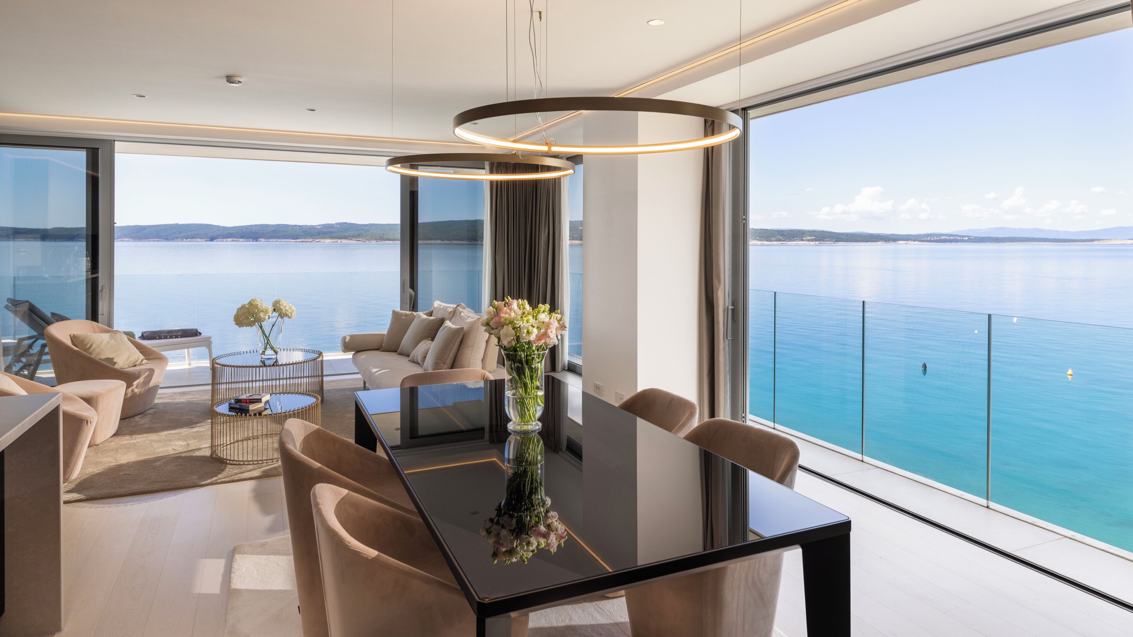 Un interior moderno con una mesa de comedor, sillas, un sofá y un ventanal con vista al mar.