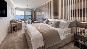 A modern hotel room with a large bed, a desk, a chair, and a view of the sea.