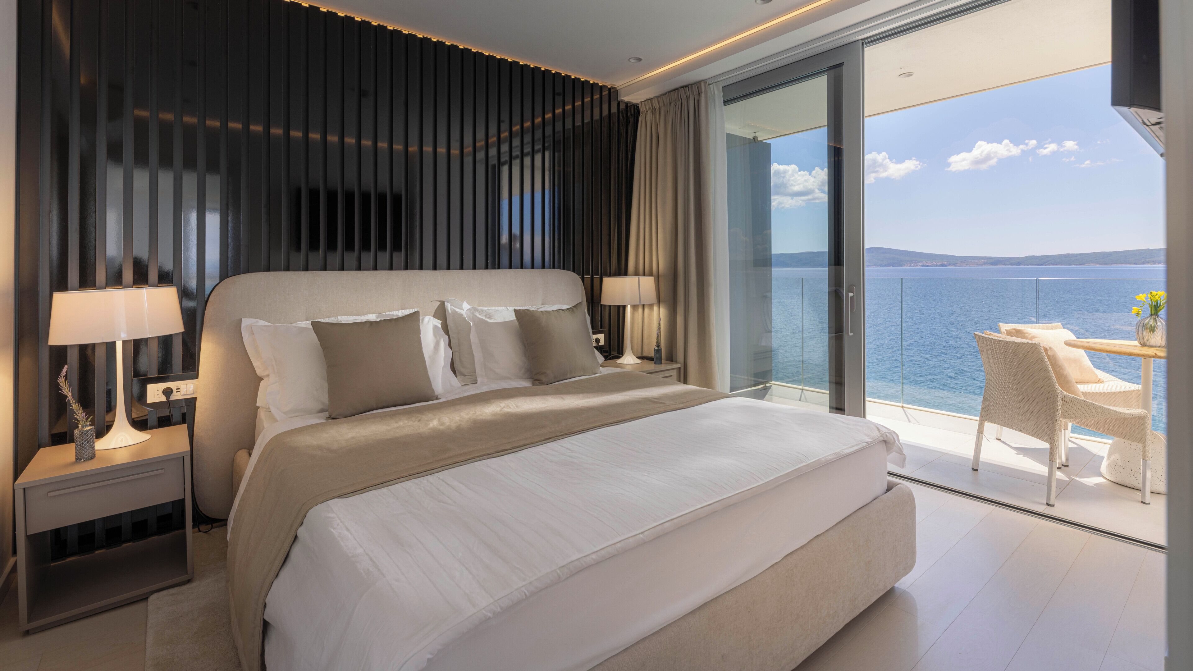 Een moderne slaapkamer met een groot bed, nachtlampjes en uitzicht op zee.