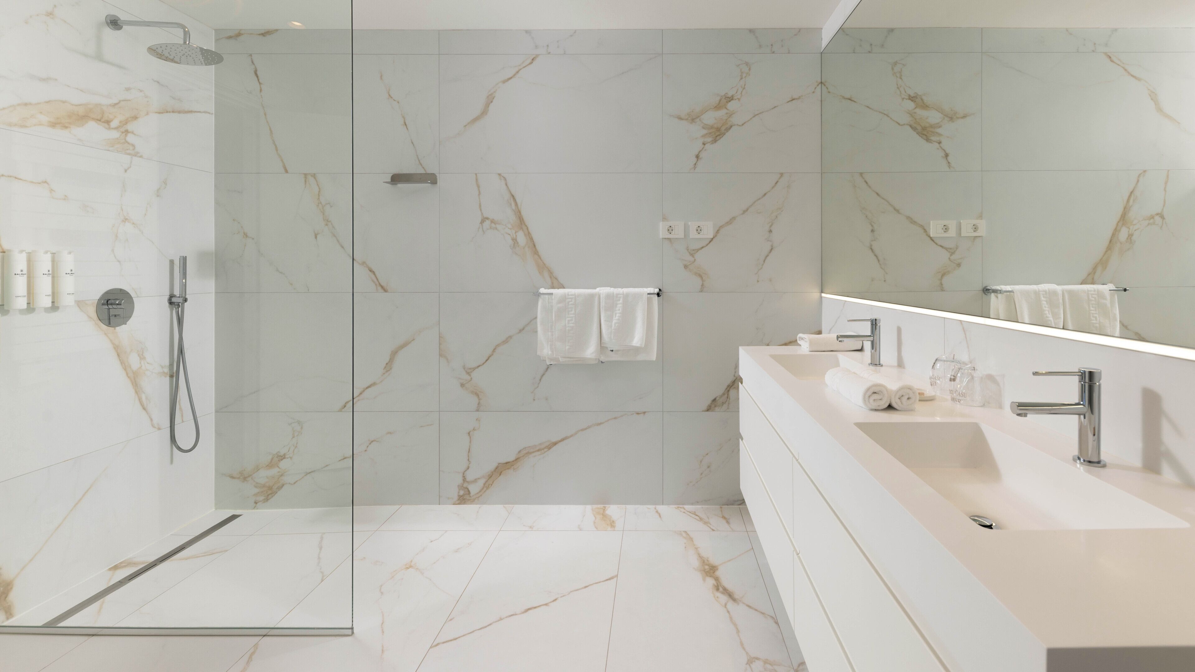 A modern bathroom with a glass-enclosed shower, a white marble wall, and a vanity with a mirror.