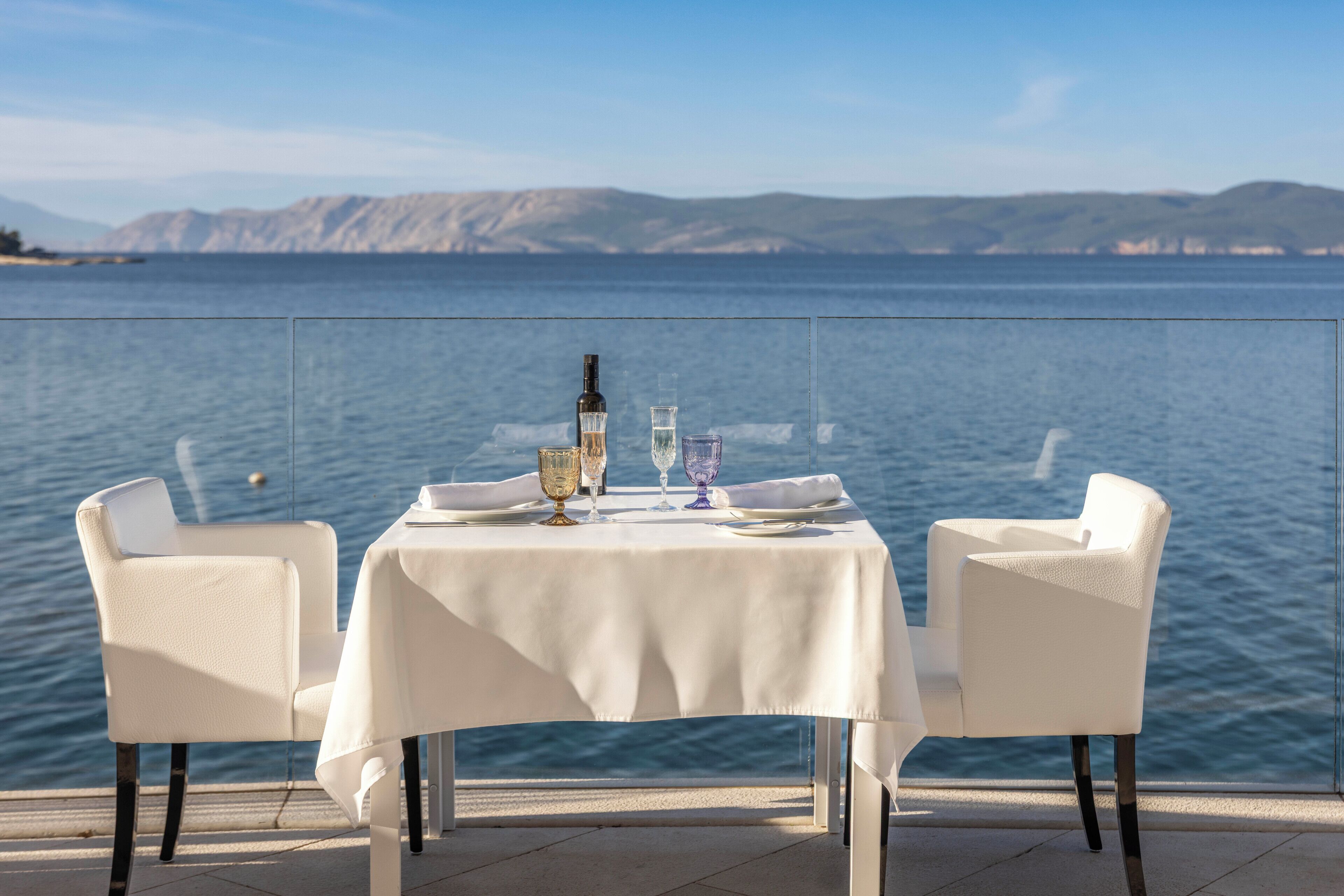 A table set for two with a view of the sea and mountains in the background.