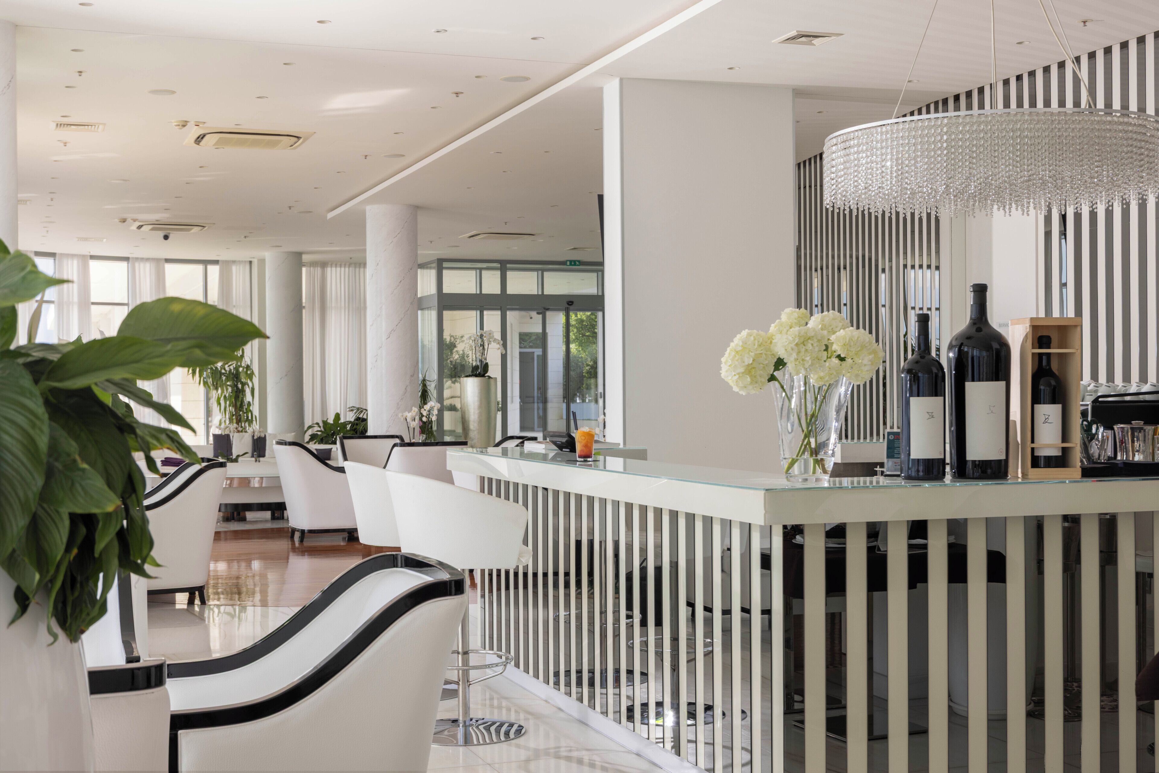Un moderno bar con una barra de vidrio, sillas blancas y una lámpara decorativa.