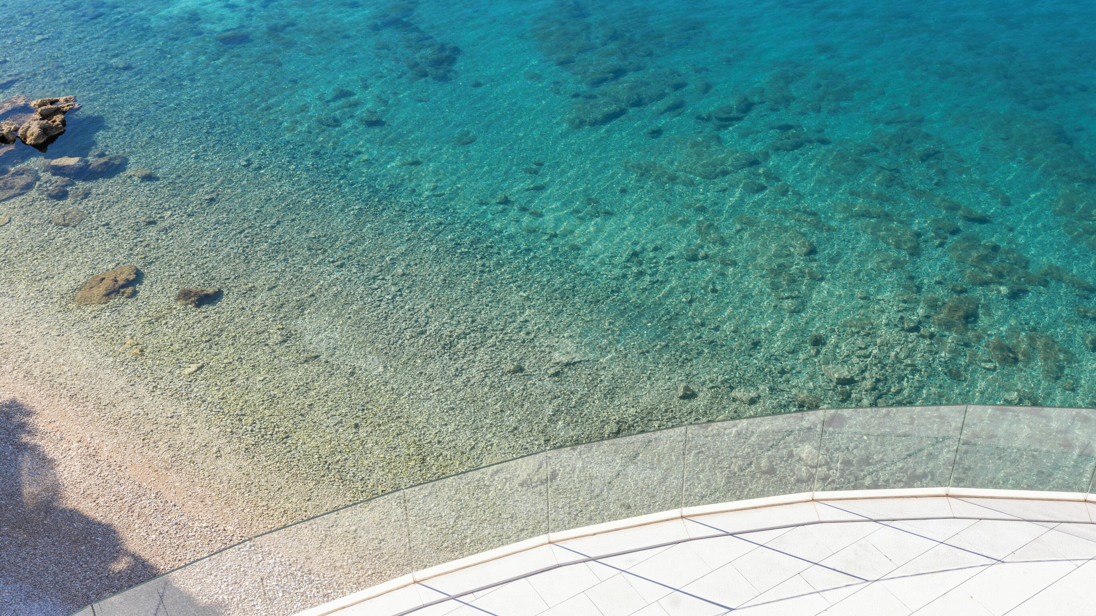 Vista despejada de una playa con piso de vidrio que permite ver el lecho marino.