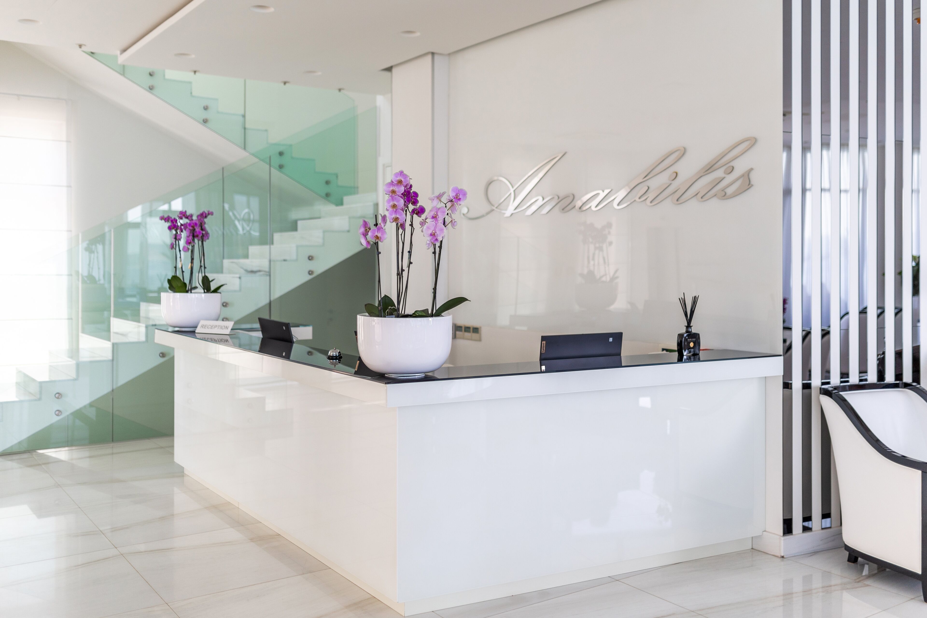 Un comptoir d’accueil au design moderne, agrémenté d’un escalier en verre et d’une plante orchidée en pot.