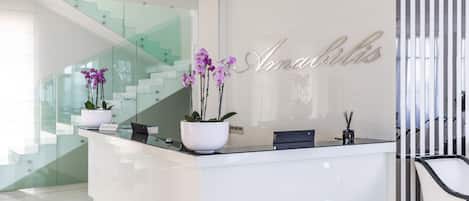 A reception desk with a modern design, featuring a glass staircase and a potted orchid plant.
