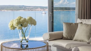Un balcon offrant une vue dégagée sur la mer et un bateau, une table en verre avec un vase de fleurs et un canapé beige agrémenté de coussins.