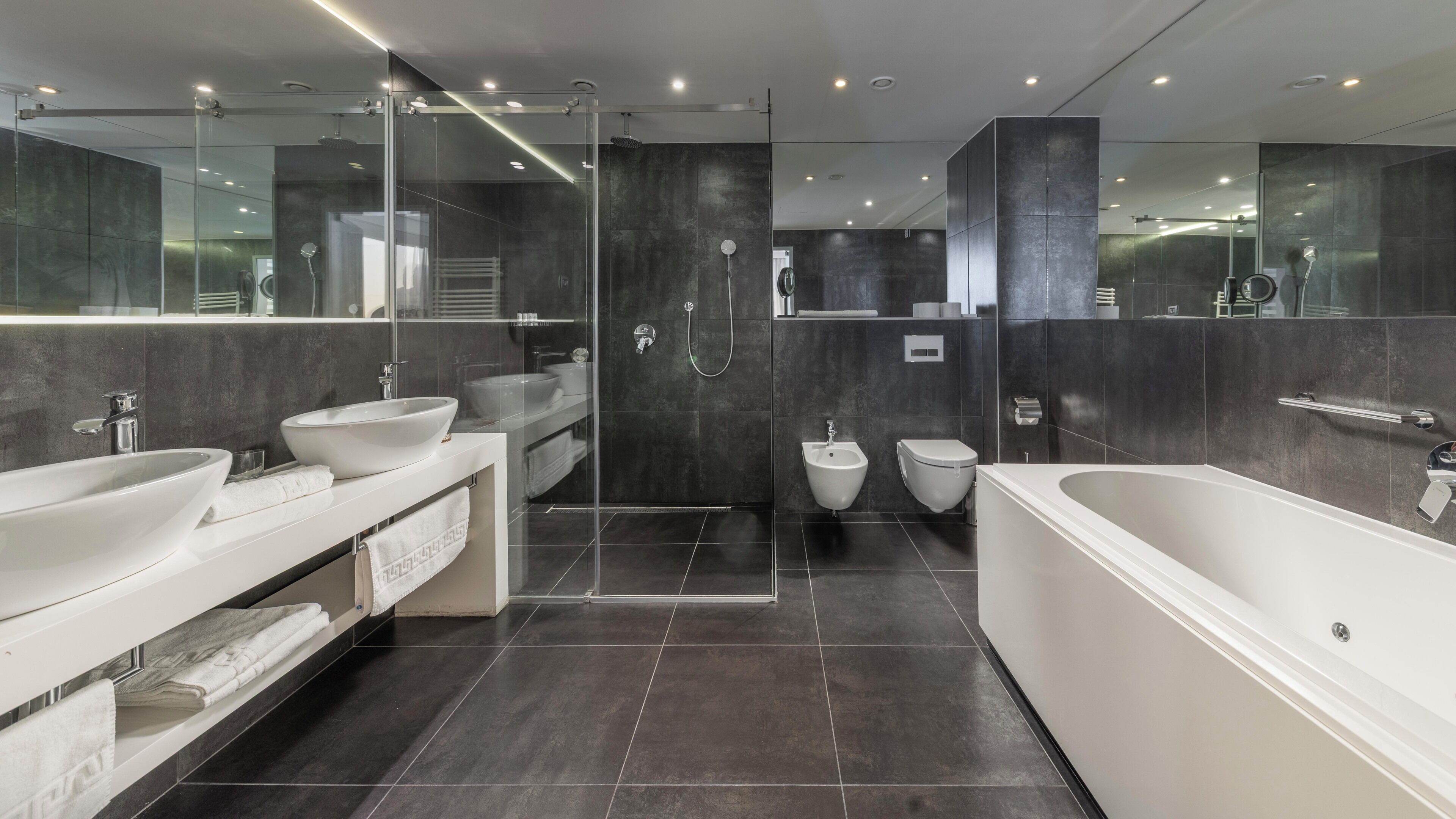 Une salle de bain moderne dotée d’une grande baignoire, de deux lavabos, d’un bidet et d’une douche séparée par une paroi en verre.