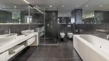 Une salle de bain moderne dotée d’une grande baignoire, de deux lavabos, d’un bidet et d’une douche séparée par une paroi en verre.