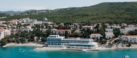 Ein Hotel an der Küste mit mehreren Etagen, einem Strand und einer Bergkulisse.