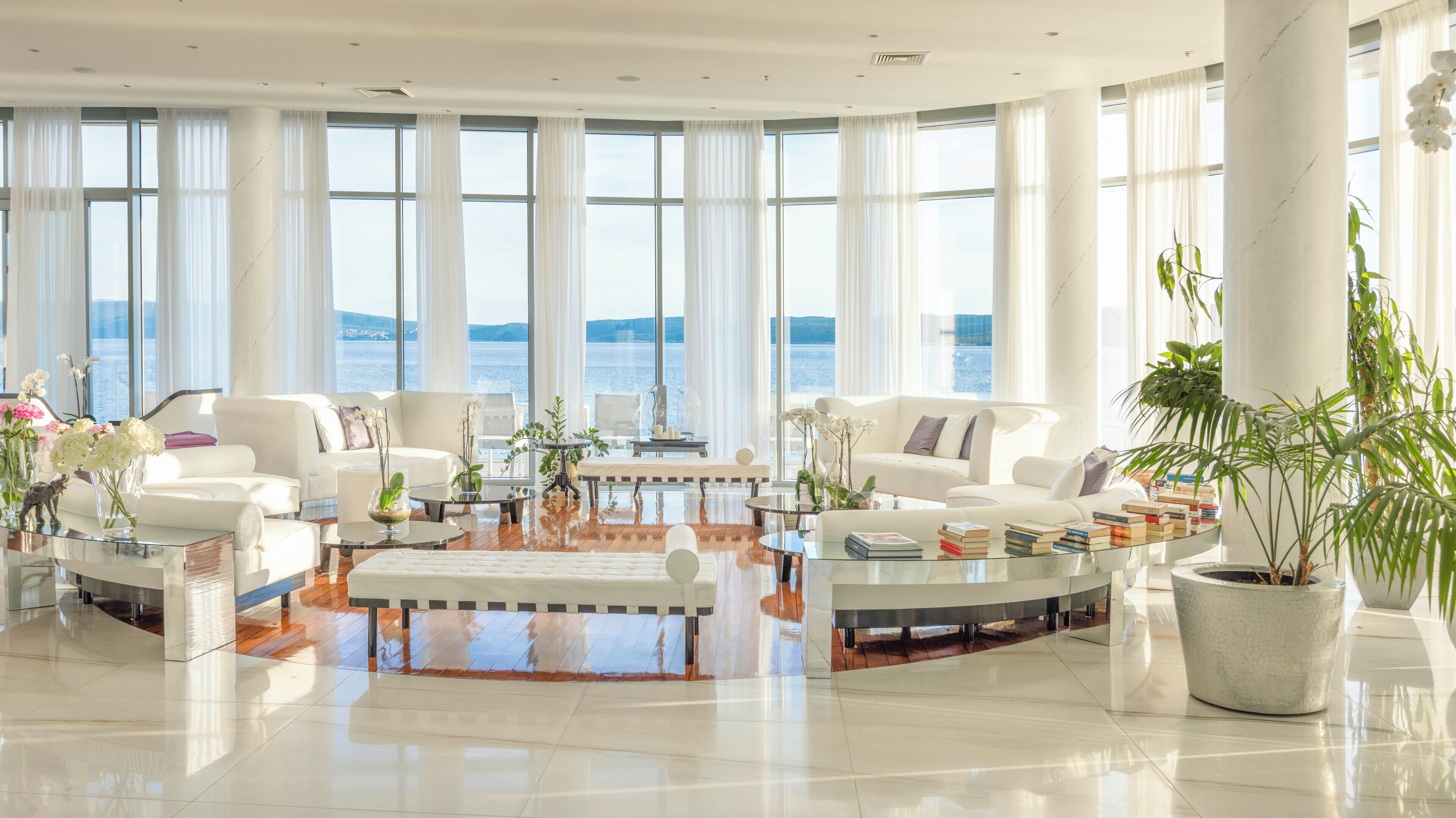 A spacious living room with a large window, a white sofa, a coffee table, and a potted plant.