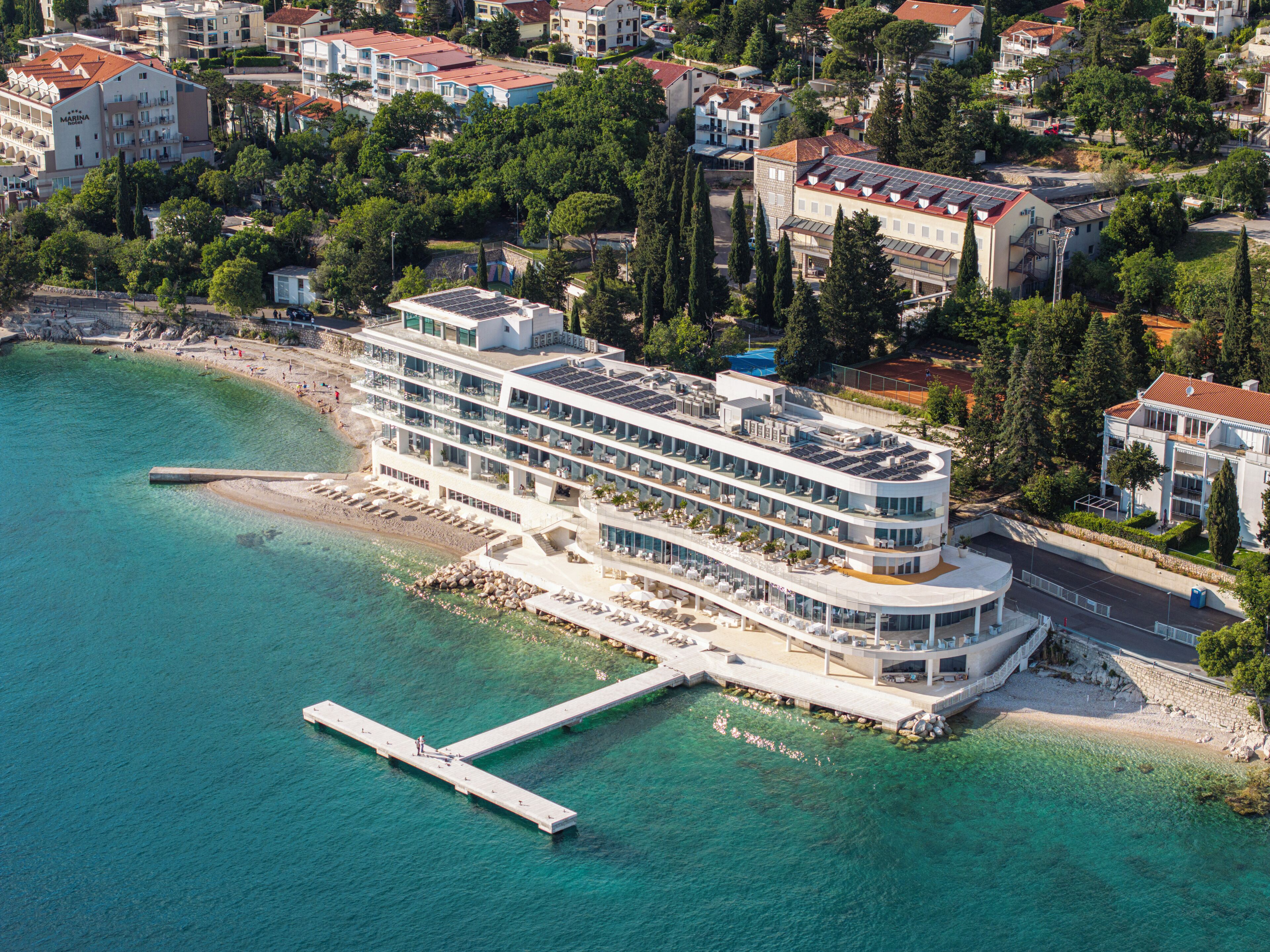 Un hotel de varios pisos con vista al agua, un muelle y un área de piscina.