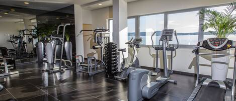 Een moderne sportschool met diverse fitnessapparaten, grote ramen en uitzicht op het water.
