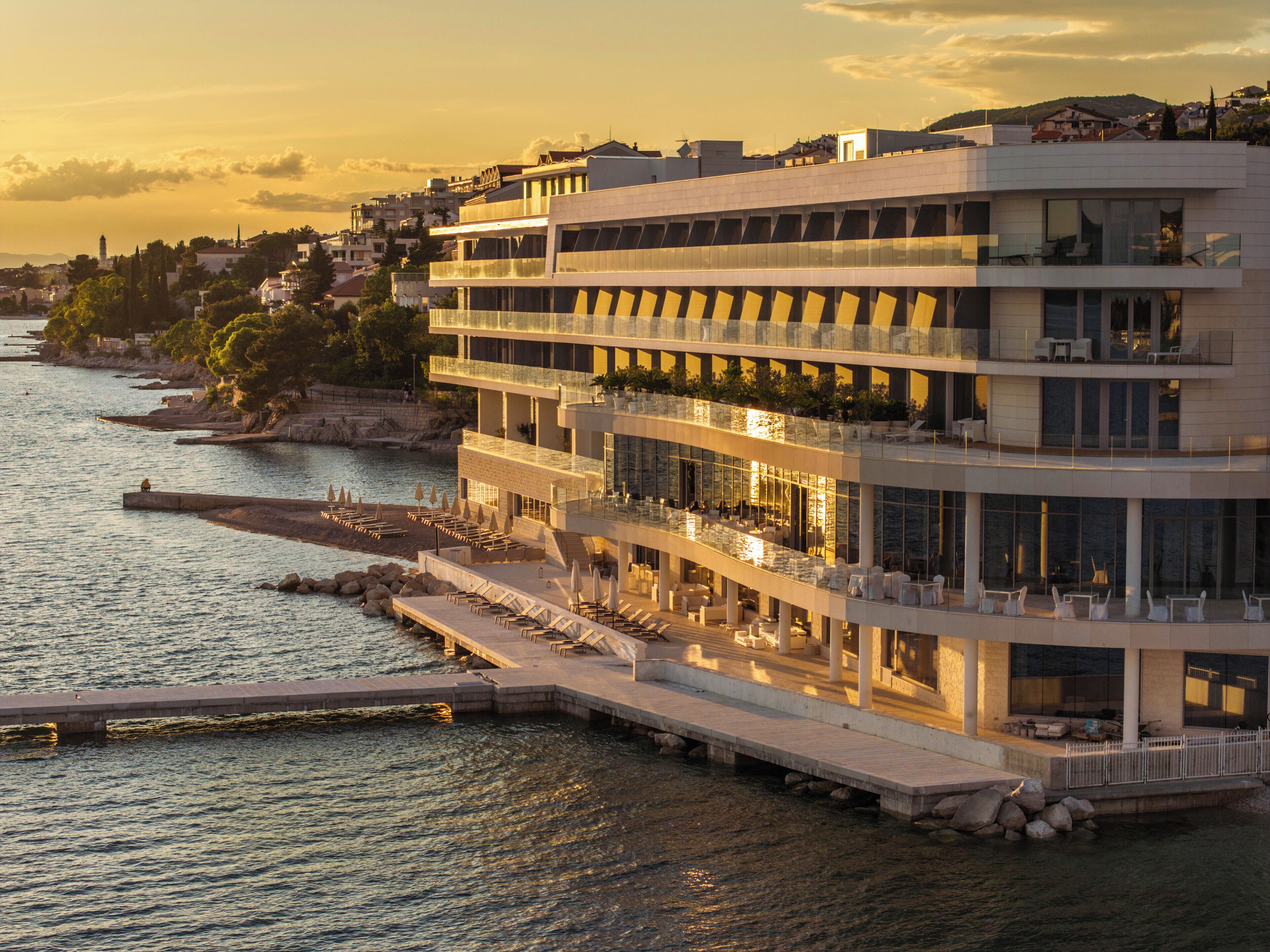 Ein mehrstöckiges Hotel mit Balkonen, Blick auf das Wasser und einer anlegenden Mole.
