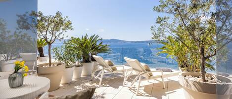 A terrace with outdoor seating, potted plants, and a view of the sea.