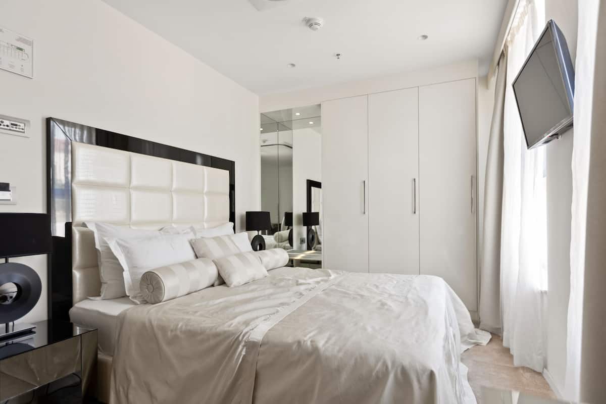 A modern bedroom with a large bed, a flat-screen TV mounted on the wall, and a wardrobe.
