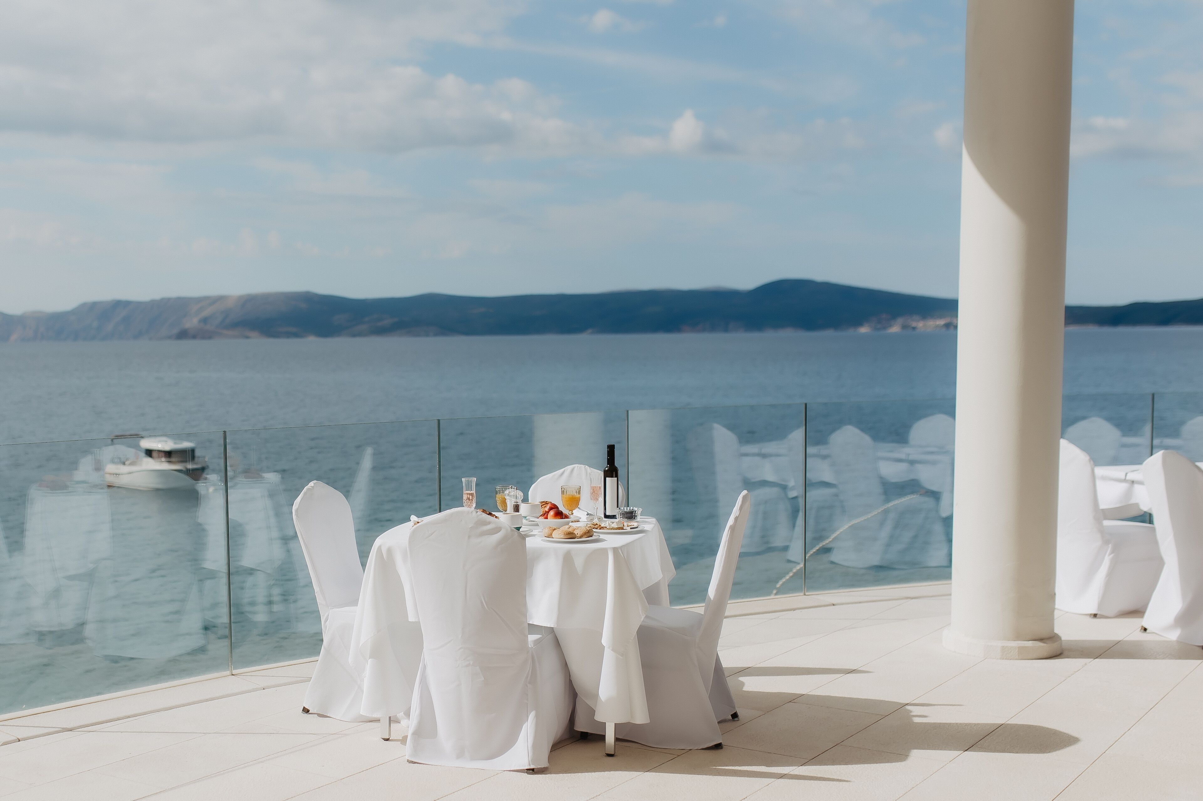 A table set for two with a view of the sea and a boat in the background.