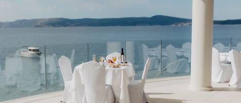 A table set for two with a view of the sea and a boat in the background.