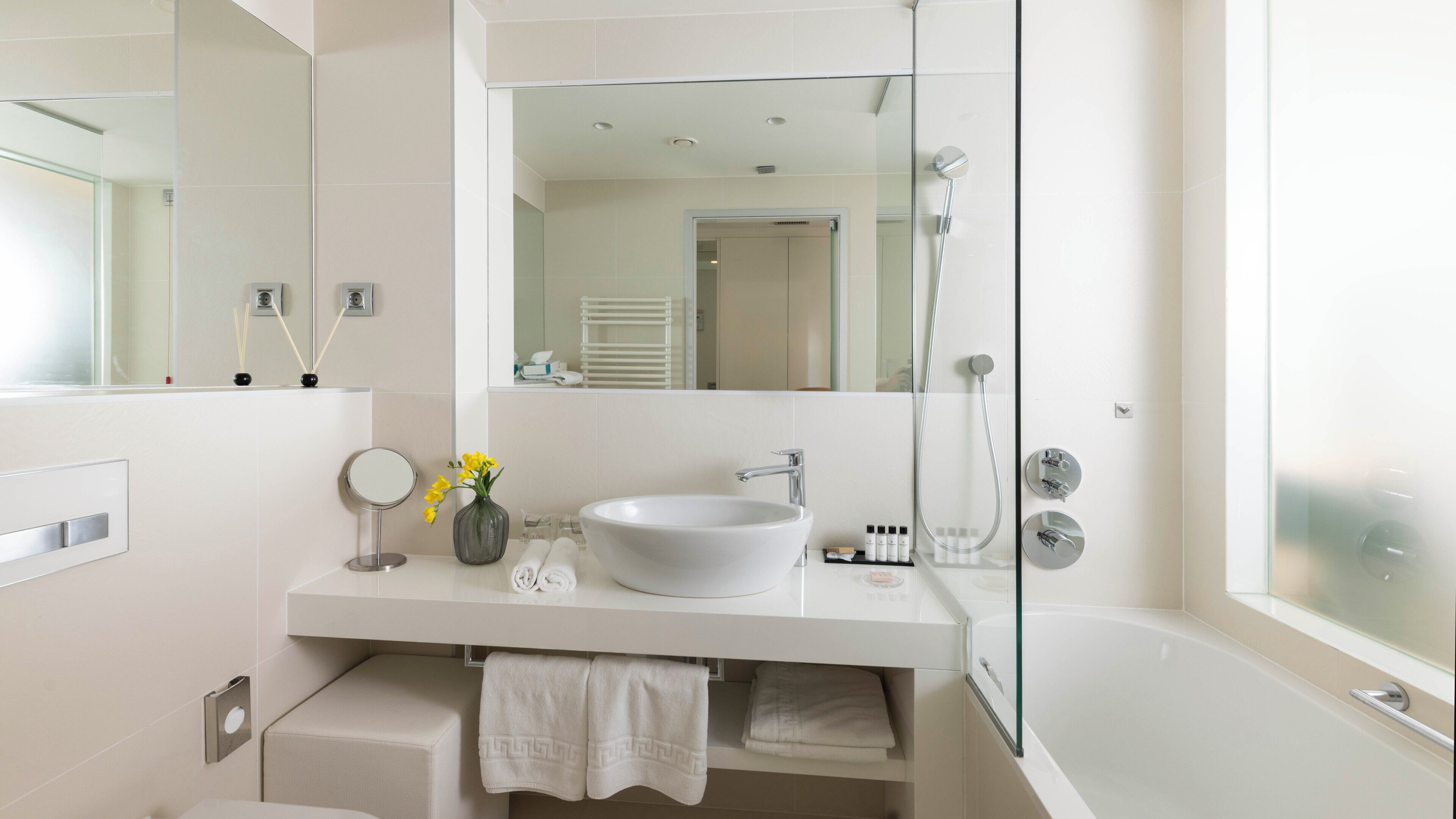 Une salle de bain moderne avec un grand miroir, un lavabo blanc, une douche en verre et une baignoire.