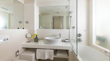 A modern bathroom with a large mirror, a white sink, a glass shower enclosure, and a bathtub.