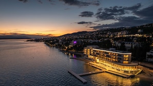 Un hôtel situé au bord de l’eau, avec un bâtiment à plusieurs étages, un quai et une vue sur le paysage urbain au crépuscule.