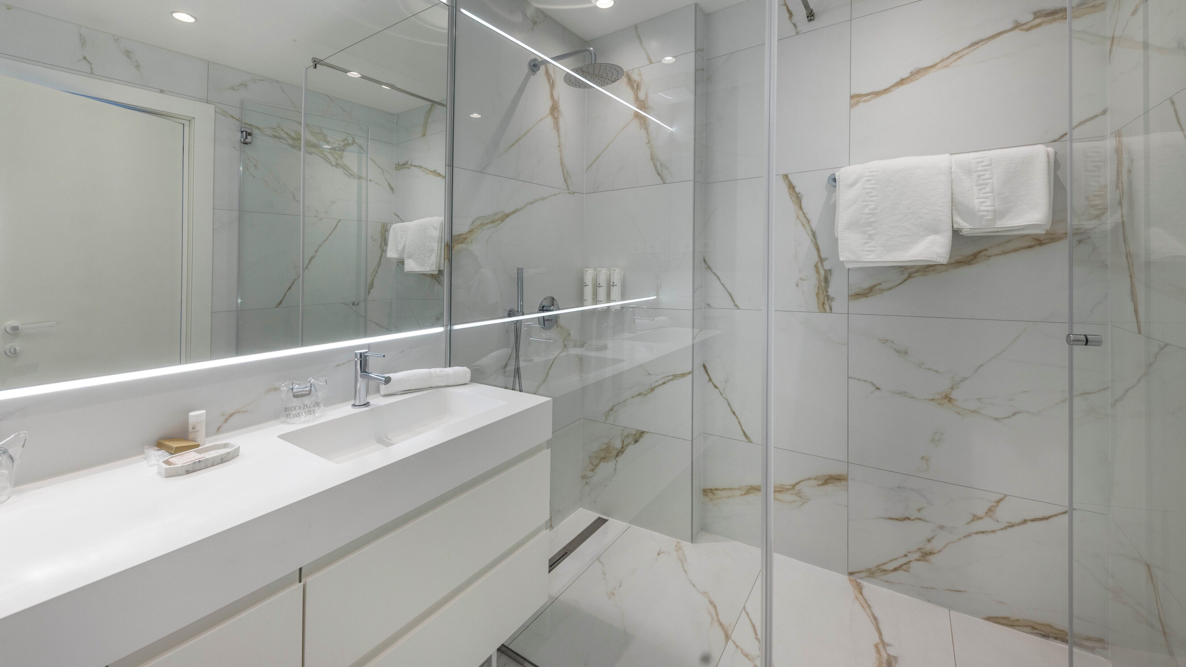A modern bathroom with a glass shower enclosure, a white sink, and marble-patterned walls.
