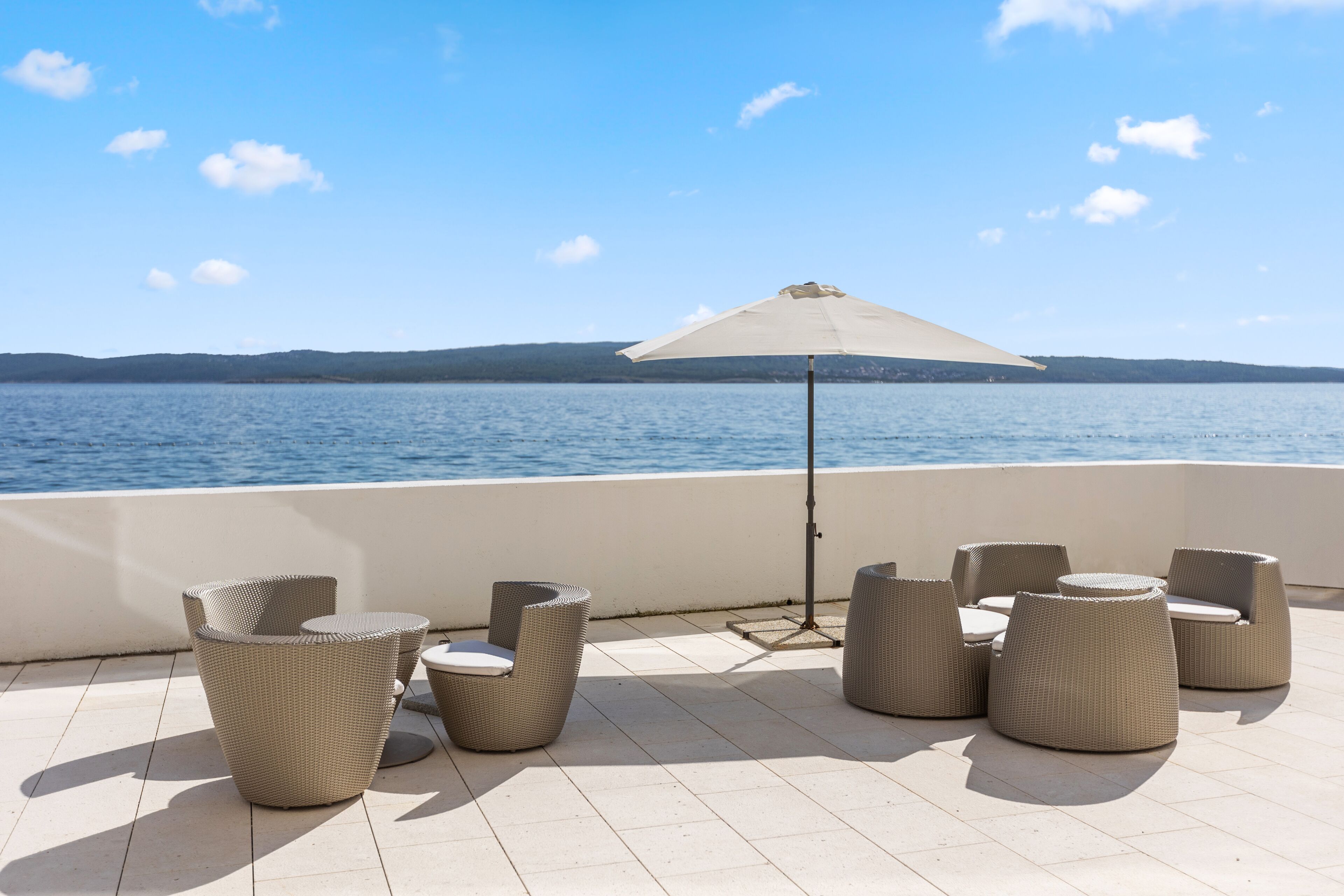 A terrace with wicker furniture and a large umbrella overlooking a body of water.
