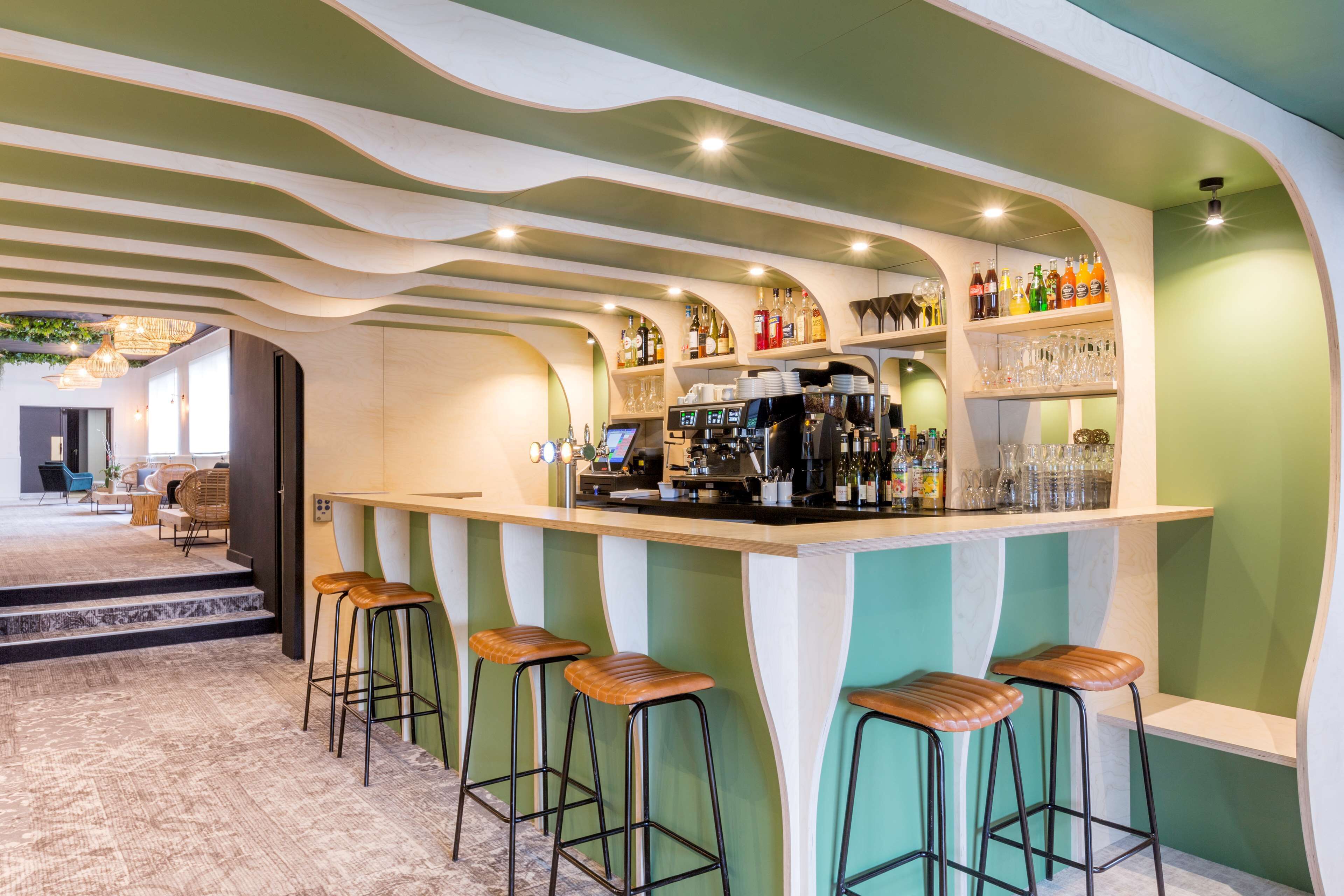 Un área de bar con taburetes, una barra y estantes llenos de botellas y vasos.