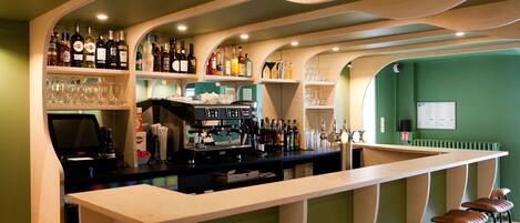Un espace bar avec un long comptoir, des tabourets, des étagères remplies de bouteilles et de verres, et une caisse enregistreuse.