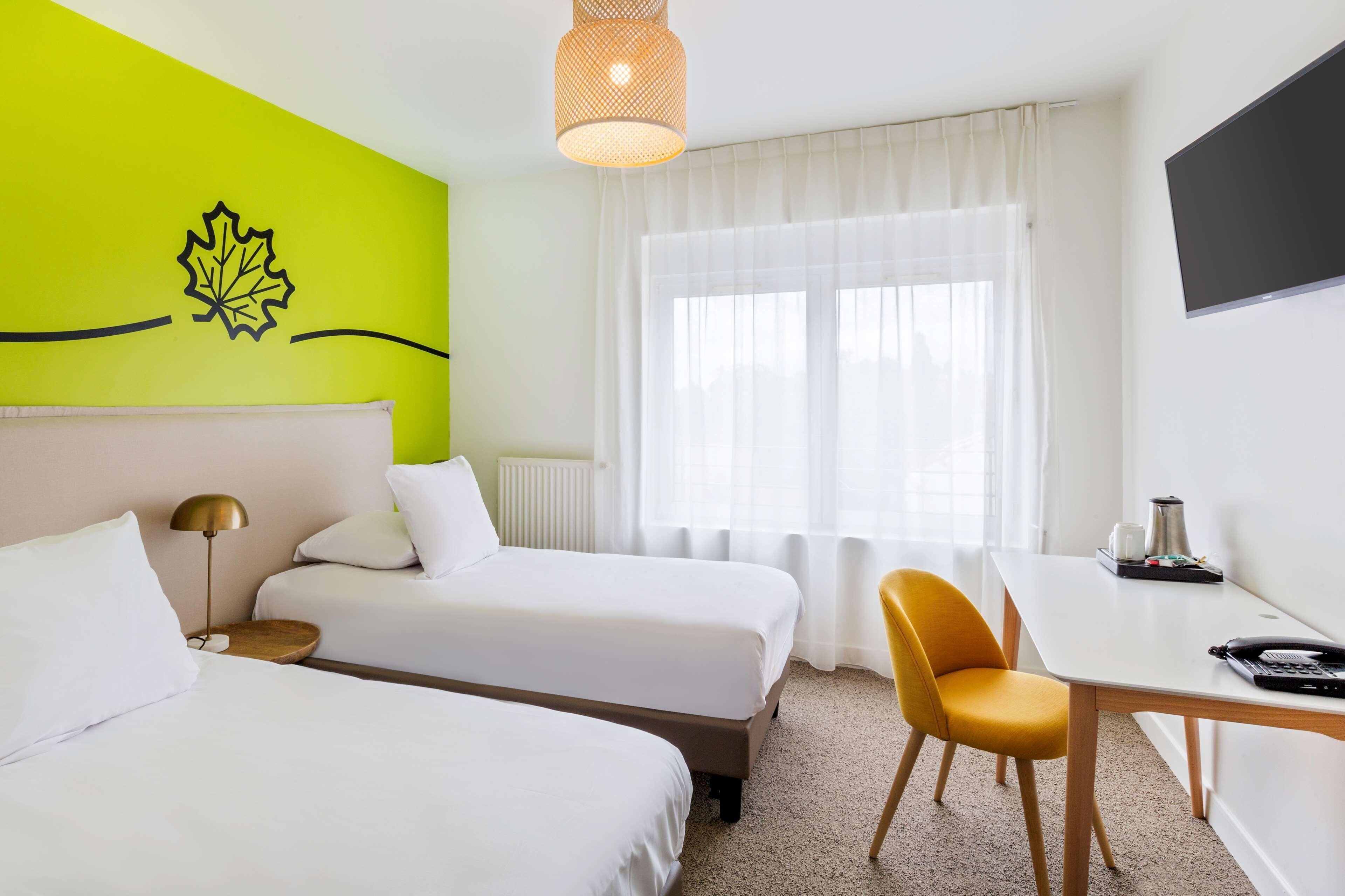 A hotel room with two beds, a desk, a chair, a television, and a window with curtains.