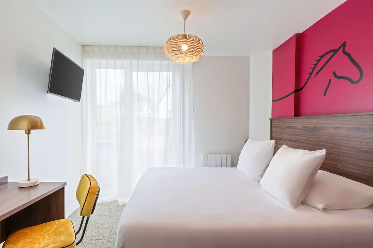 Habitación de hotel con cama, escritorio, silla, televisor y un mural de un caballo en la pared.
