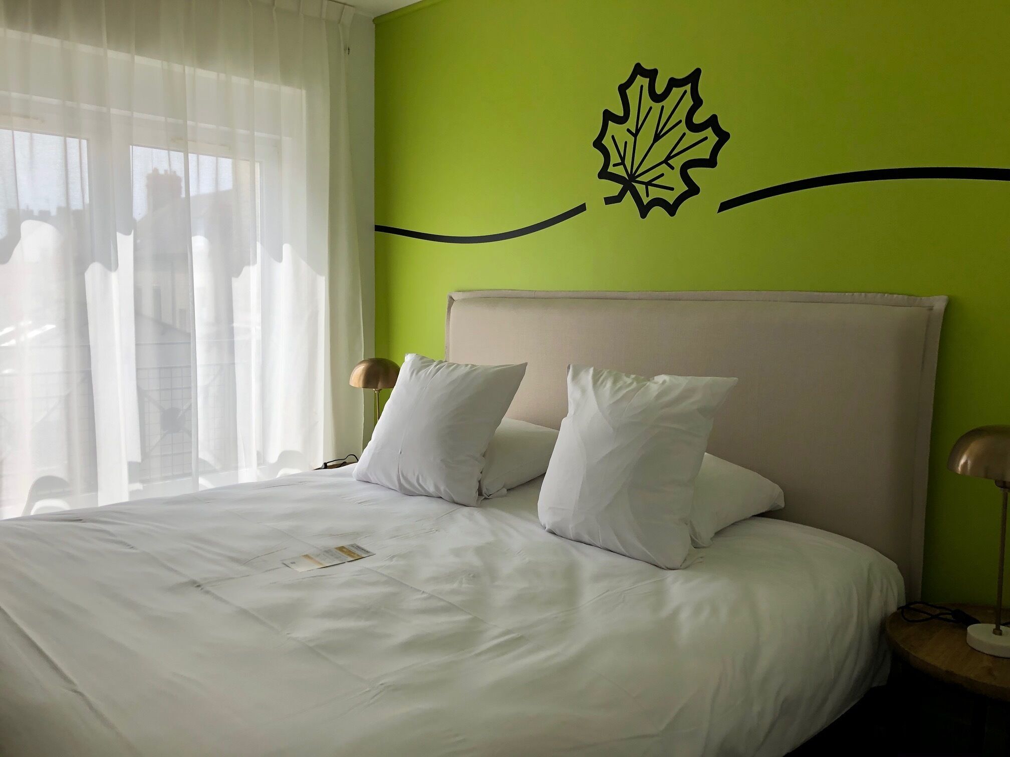 Een opgemaakt bed met witte lakens, een groene accentmuur en een bladsticker.