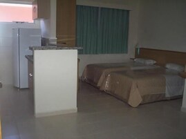 A hotel room with a kitchenette, a bed with a headboard, and a window with curtains.