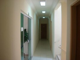 A narrow, well-lit hallway with a tiled floor, leading to a door at the end.