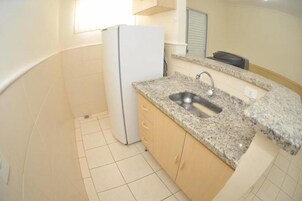A small kitchen with a white refrigerator, granite countertop, and a sink.
