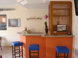 A bar area with a counter, stools, a small shelf with decorative items, and a mirror.