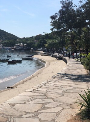 A coastal walkway with boats docked nearby, a sandy beach, and a stone-paved path. - Calador Búzios Hotel (Búzios)