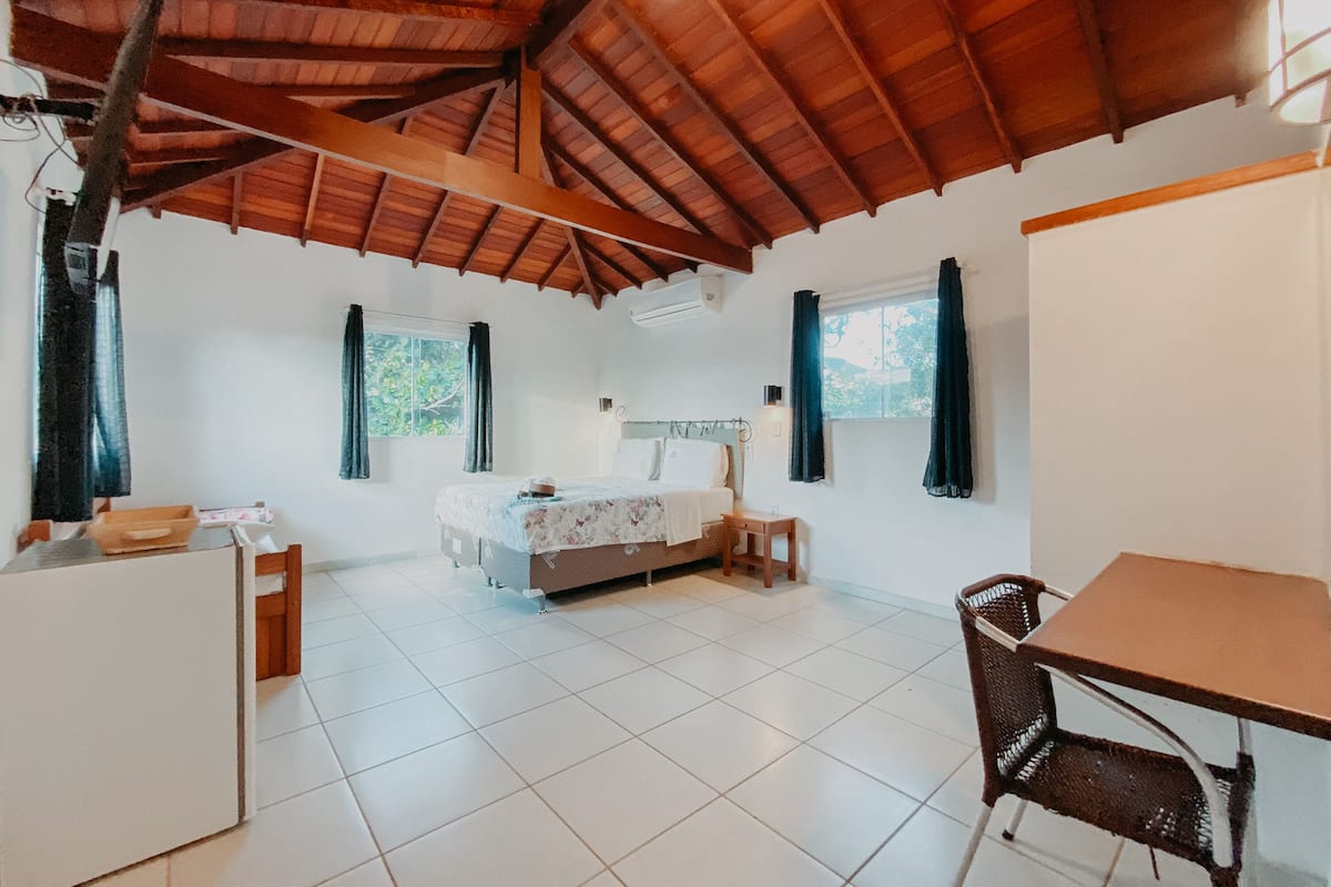 Um quarto com uma cama, uma mesa pequena, uma cadeira e uma janela com cortinas.