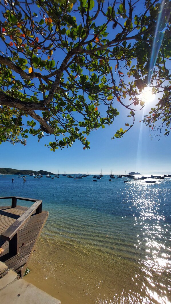 A wooden pier extending into clear blue water with boats anchored in the distance. - Calador Búzios Hotel (Búzios)