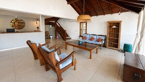 Uma sala de estar ampla com teto alto, um balcão de recepção de madeira, um sofá com almofadas, uma mesa de centro e uma estante de livros.