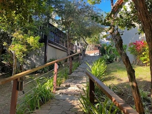 A stone pathway leading to a building with a wooden railing, surrounded by greenery and trees. - Calador Búzios Hotel (Búzios)