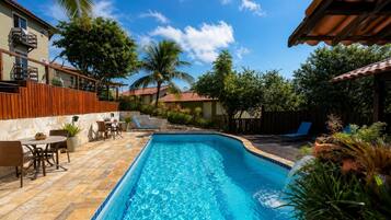 A swimming pool with a wooden deck, lounge chairs, and a patio area with a table and chairs.