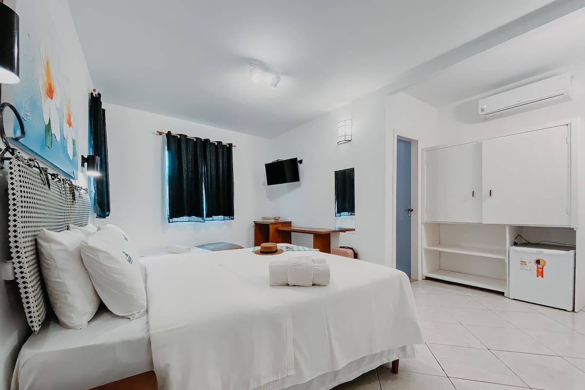 Quarto de hotel com cama, escrivaninha, guarda-roupa e televisão na parede.